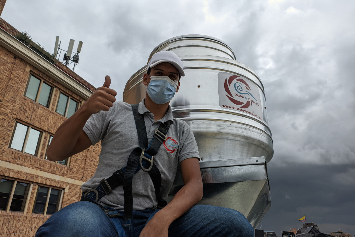 Técnico de instalación mostrando ventilador tipo hongo en cubierta de edificio, con logo de Ductos & Ventilación visible.